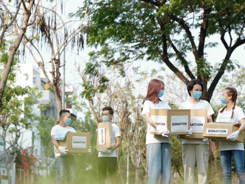 Group of young volunteers in medical masks gathering in park to collect donations for charitable foundation